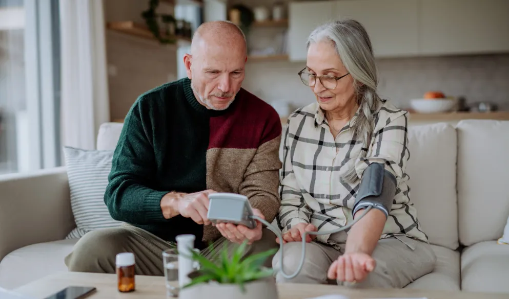 A senior couple at home measuring blood pressure with pills on table