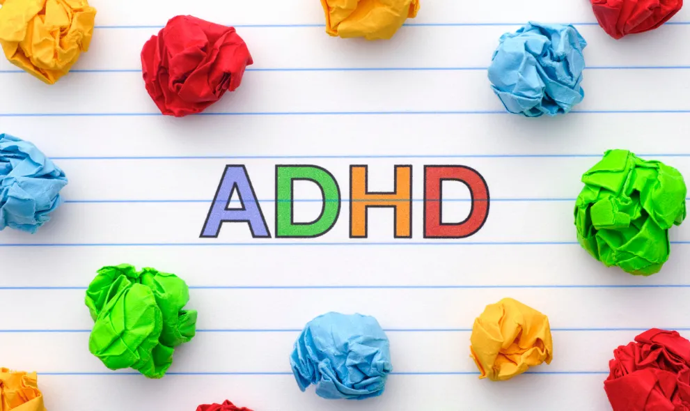 Abbreviated ADHD on notebook sheet with some colorful crumpled paper balls around it
