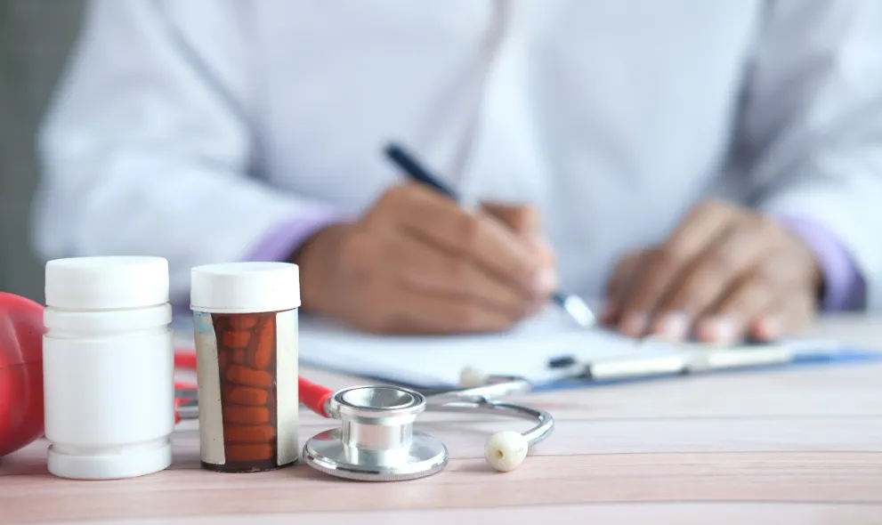 Doctor writing a prescription with bottles of pills