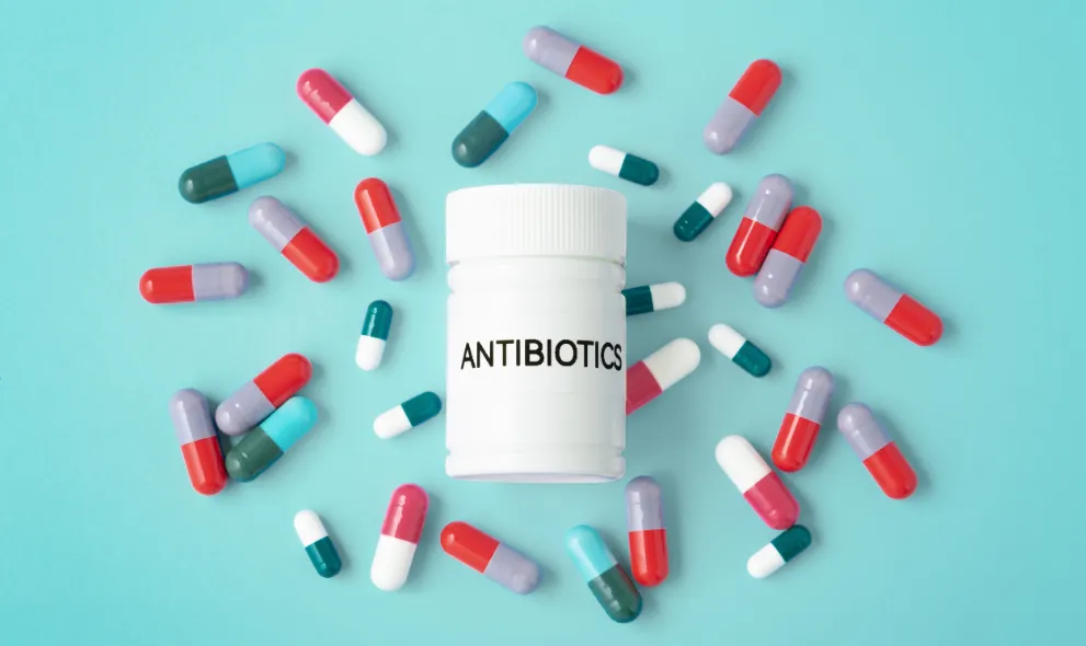Heap of capsules with antibiotic medicine bottle on green background