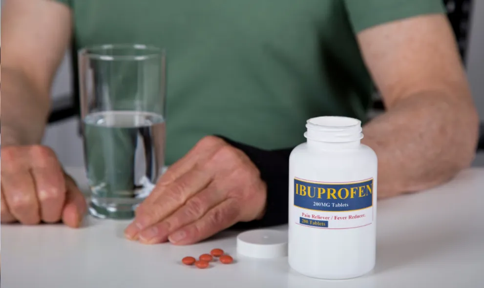 Man sitting with bottle of ibuprofen and glass of water