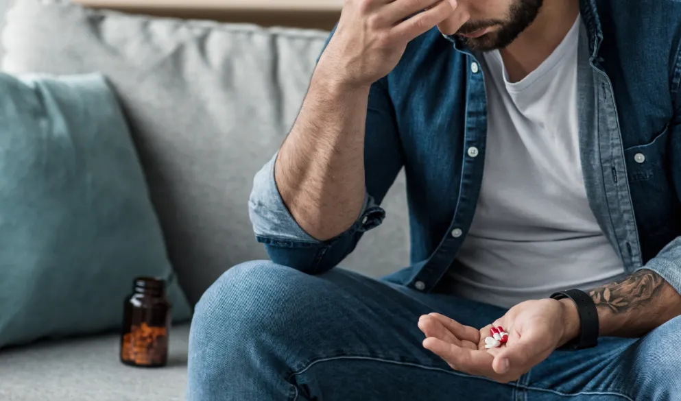Unhappy adult male holding medication in palm while sitting on couch